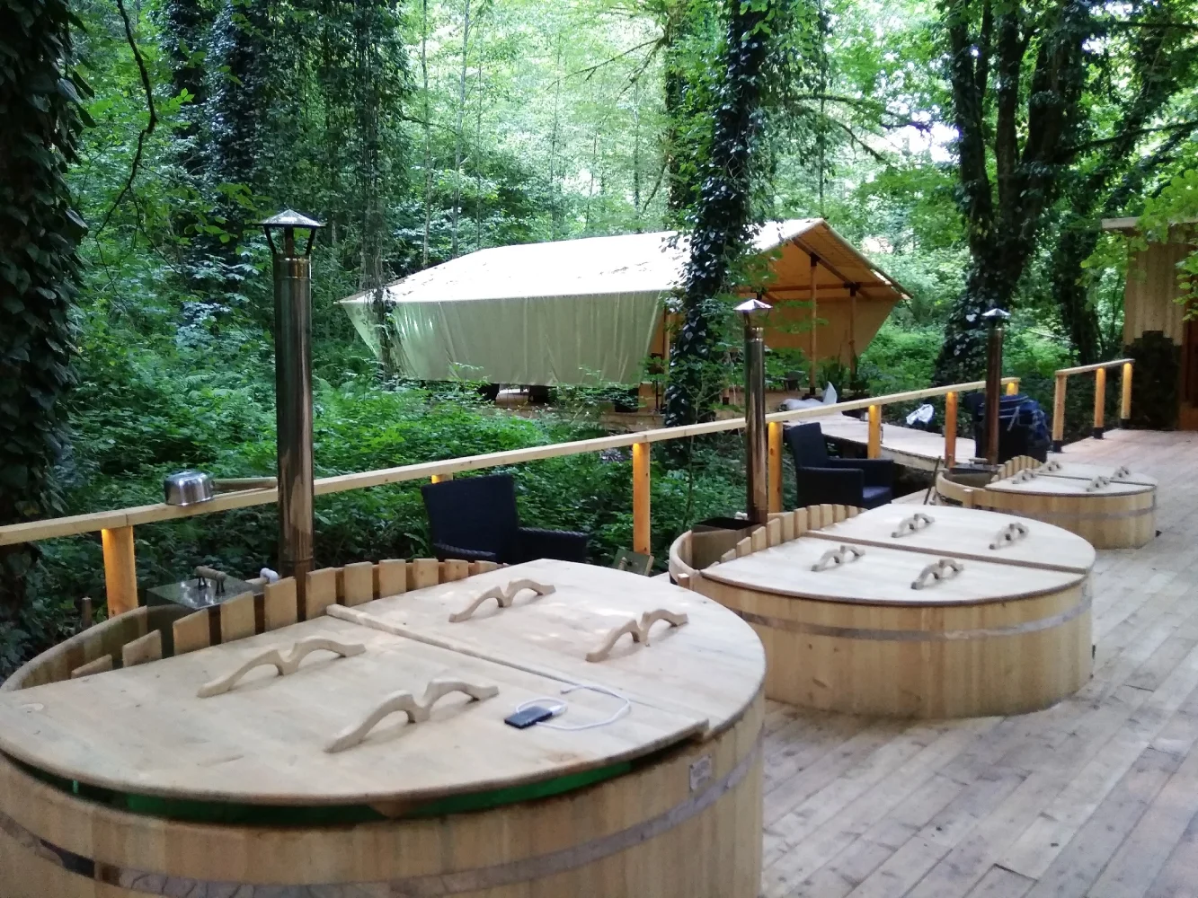 Spoljašnja terasa Pati modela sa drvenim spa kadama i servisnim elementima u šumskom okruženju.